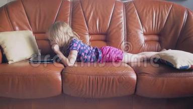 一个可爱的金发小女孩穿着所有粉红色的侧视图躺在沙发上，在平板电脑上玩游戏。 4k